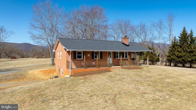 ranch-style house featuring a mountain view, covered porch, a front yard, brick siding, and a chimney