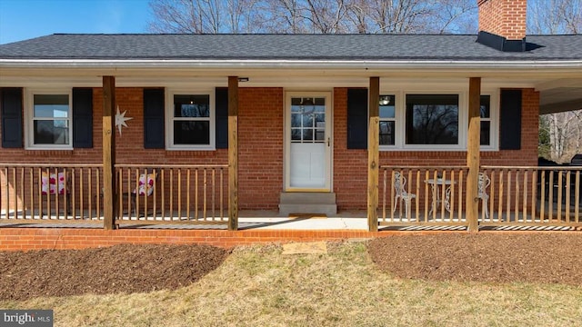 view of front facade featuring brick siding, covered porch, and roof with shingles