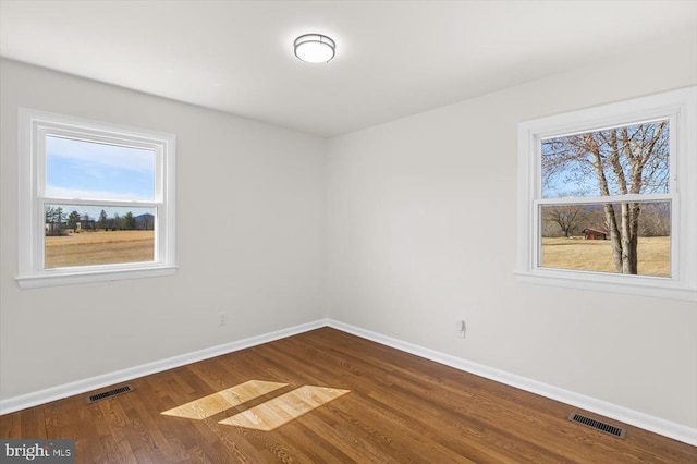 spare room featuring dark wood-type flooring, baseboards, and visible vents