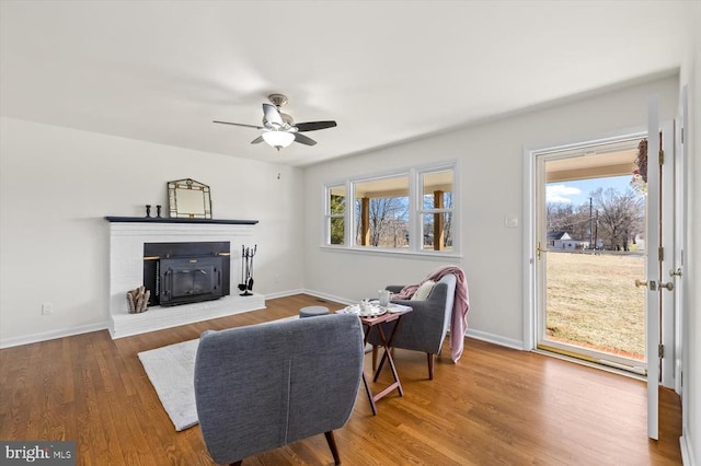 living room with ceiling fan, wood finished floors, baseboards, and a fireplace with raised hearth