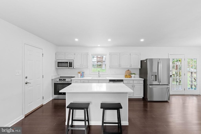 kitchen with appliances with stainless steel finishes, a sink, a breakfast bar area, light countertops, and dark wood-type flooring