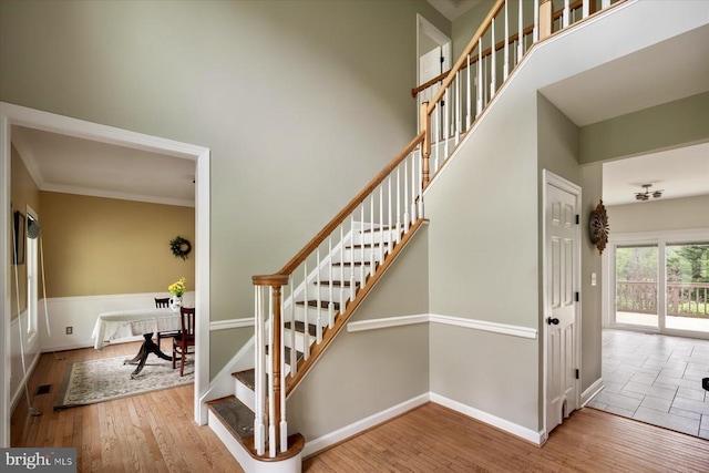 stairway featuring a towering ceiling, crown molding, wood finished floors, and baseboards