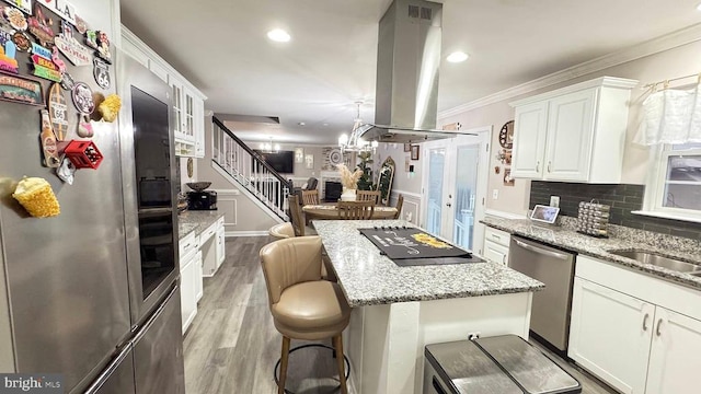 kitchen with a breakfast bar, appliances with stainless steel finishes, white cabinetry, island range hood, and a kitchen island