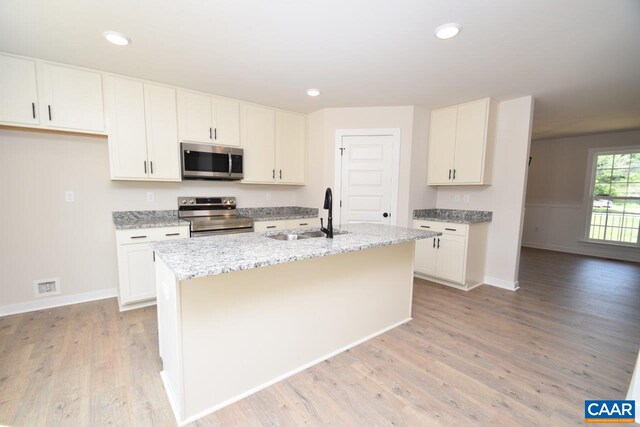 kitchen featuring a sink, stainless steel appliances, an island with sink, light stone countertops, and light wood-style floors