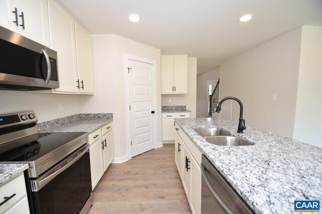 kitchen featuring a sink, stainless steel appliances, white cabinets, light wood-type flooring, and light stone countertops