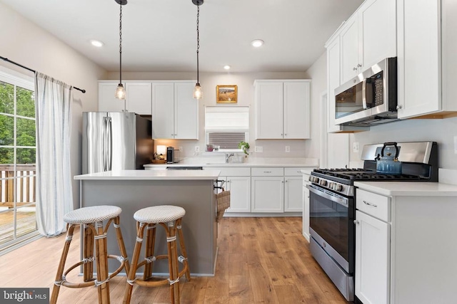kitchen featuring stainless steel appliances, a kitchen island, white cabinetry, light wood-style floors, and light countertops