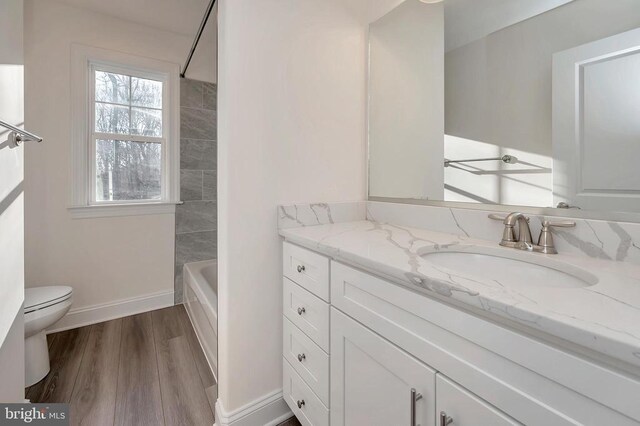  - bathroom featuring vanity, toilet, wood finished floors, a tub to relax in, and baseboards