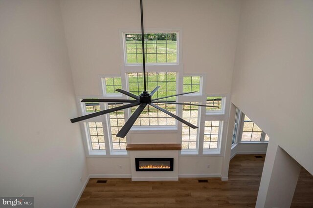  - unfurnished living room featuring a towering ceiling, baseboards, wood finished floors, and a glass covered fireplace