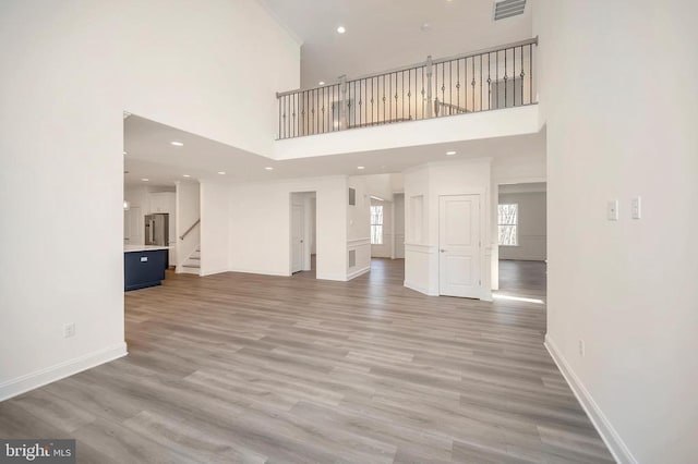  - unfurnished living room with stairs, a high ceiling, baseboards, light wood-type flooring, and recessed lighting