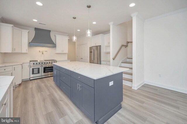  - kitchen with custom range hood, high quality appliances, white cabinets, light wood finished floors, and ornamental molding