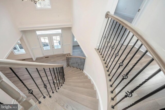  - stairs with french doors, a high ceiling, wood finished floors, a chandelier, and baseboards