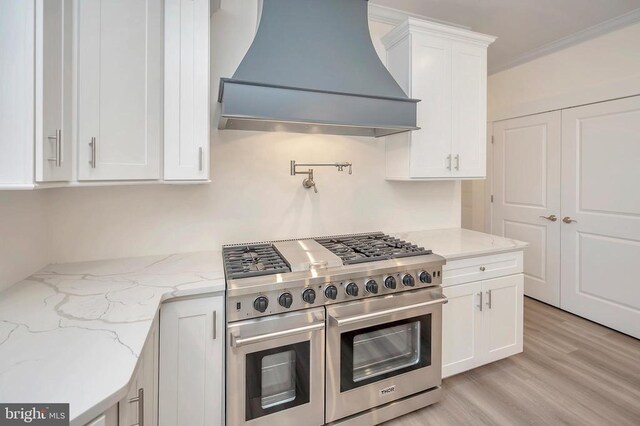  - kitchen with double oven range, custom exhaust hood, white cabinetry, light wood finished floors, and crown molding