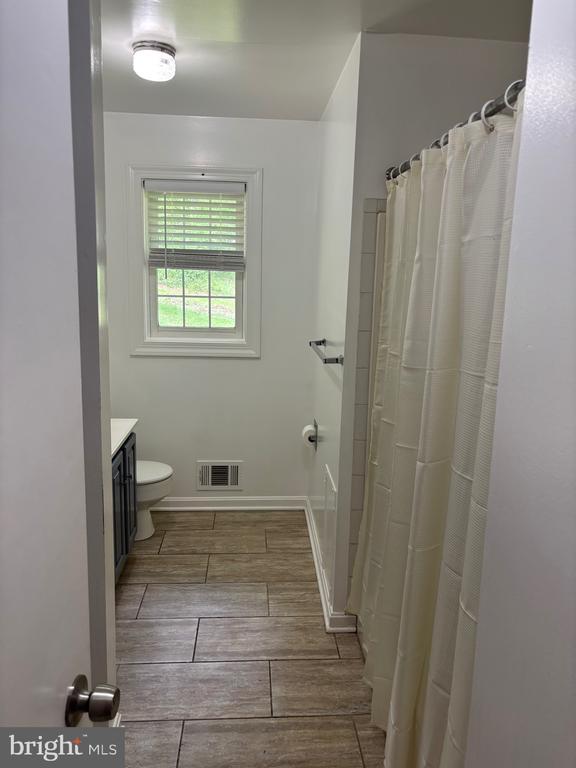  - bathroom featuring wood finish floors, vanity, toilet, and curtained shower