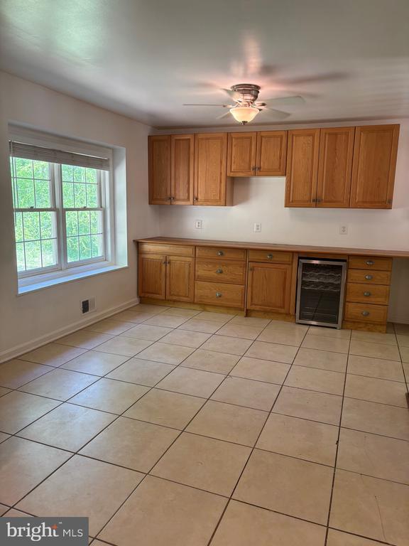  - kitchen with beverage cooler, brown cabinets, light tile patterned floors, ceiling fan, and baseboards