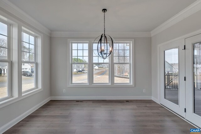 unfurnished dining area with an inviting chandelier, ornamental molding, a wealth of natural light, and dark wood-type flooring
