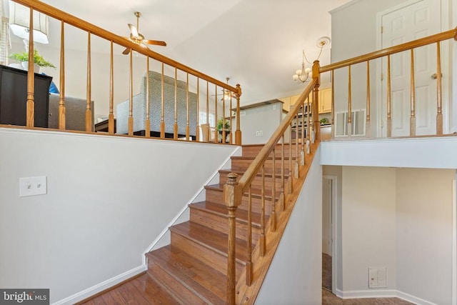  - staircase with ceiling fan, a chandelier, a high ceiling, and wood finished floors