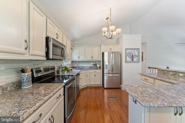  - kitchen with appliances with stainless steel finishes, a chandelier, backsplash, vaulted ceiling, and dark wood-style flooring