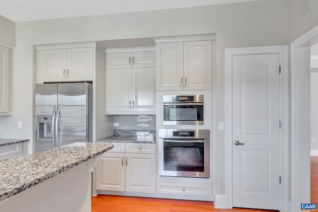 kitchen featuring light stone counters, stainless steel fridge with ice dispenser, white cabinets, and decorative backsplash