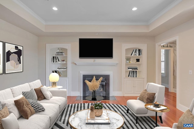 living room featuring a tray ceiling, built in features, wood finished floors, and a fireplace with flush hearth