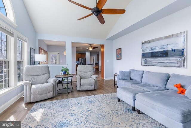 living room with ceiling fan, wood finished floors, baseboards, and high vaulted ceiling