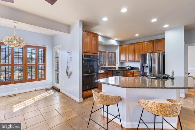 kitchen featuring stainless steel appliances, a kitchen breakfast bar, recessed lighting, dark stone counters, and a sink