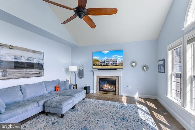 living area with a glass covered fireplace, wood finished floors, ceiling fan, baseboards, and high vaulted ceiling