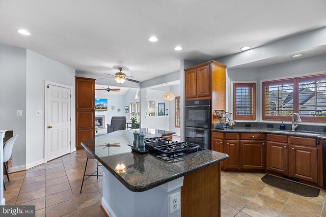 kitchen with a sink, black appliances, ceiling fan, a kitchen island, and dark stone countertops