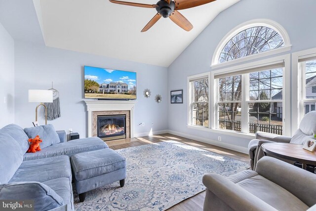 living area with healthy amount of natural light, a ceiling fan, high vaulted ceiling, baseboards, and a fireplace with flush hearth