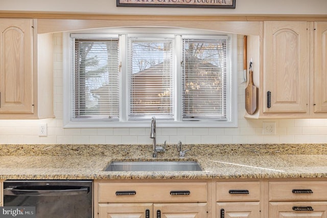 kitchen view of dishwasher, light brown cabinets, a sink, tasteful backsplash, and light stone counters