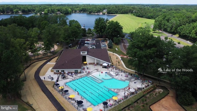 drone / aerial view of a forest, a pool area, and a large body of water