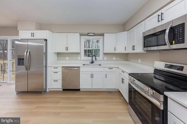 kitchen with sink, light hardwood / wood-style floors, white cabinets, and appliances with stainless steel finishes