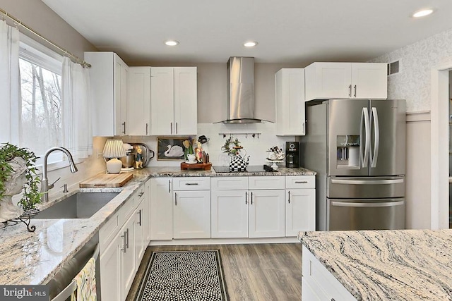 kitchen with light stone countertops, visible vents, stainless steel fridge with ice dispenser, wall chimney exhaust hood, and white cabinets