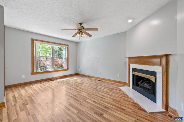 unfurnished living room with light wood-style flooring, a tiled fireplace, a textured ceiling, baseboards, and ceiling fan