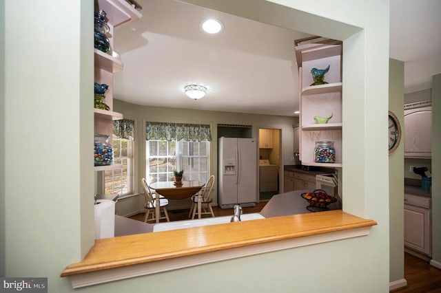 kitchen with white refrigerator with ice dispenser, open shelves, and washer / dryer