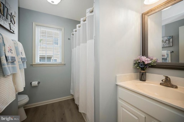 bathroom featuring wood finished floors, toilet, vanity, and baseboards
