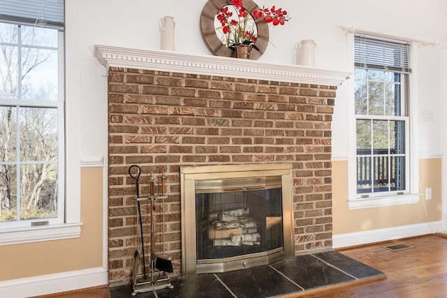 room details featuring baseboards, a brick fireplace, visible vents, and wood finished floors