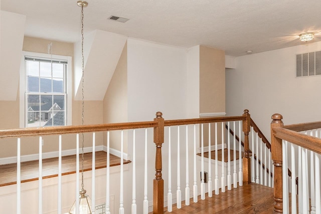 hallway featuring an upstairs landing, a textured ceiling, visible vents, and wood finished floors