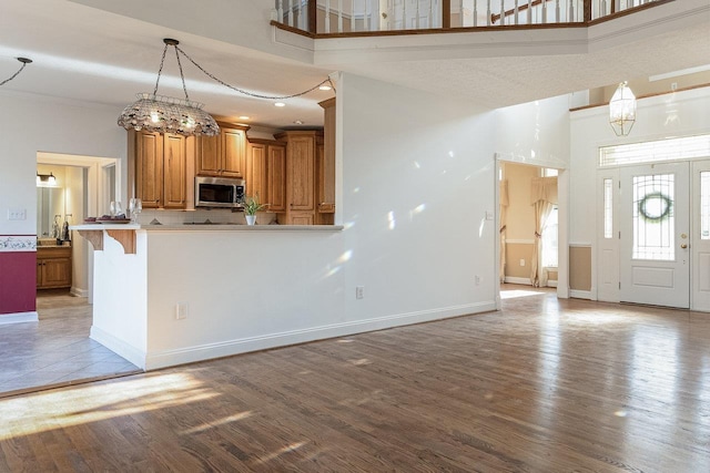 kitchen with stainless steel microwave, wood finished floors, a high ceiling, and brown cabinets