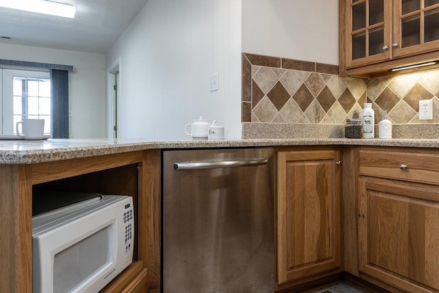kitchen featuring glass insert cabinets, dishwasher, light stone counters, white microwave, and brown cabinets