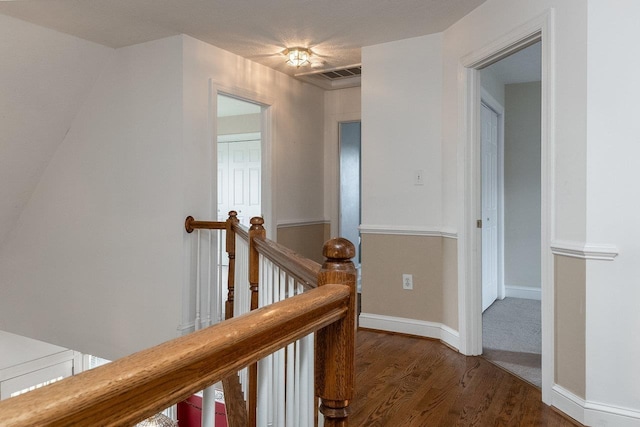 hall featuring wood finished floors, visible vents, and an upstairs landing