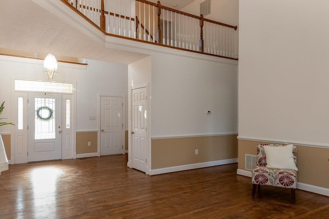 foyer entrance with a high ceiling, baseboards, visible vents, and wood finished floors