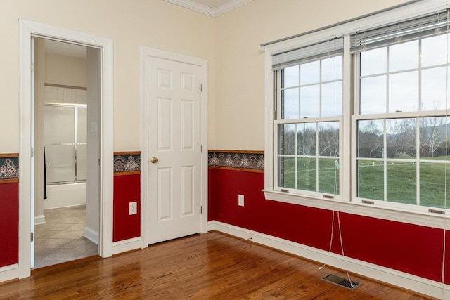 unfurnished bedroom featuring wood finished floors, crown molding, visible vents, baseboards, and ensuite bath
