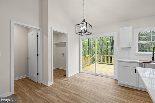 unfurnished dining area with a sink, light wood-style floors, a chandelier, baseboards, and lofted ceiling