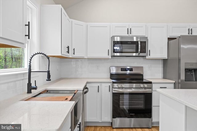 kitchen with appliances with stainless steel finishes, white cabinets, backsplash, and vaulted ceiling