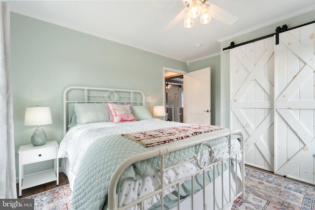 bedroom with ceiling fan, a barn door, wood finished floors, and crown molding