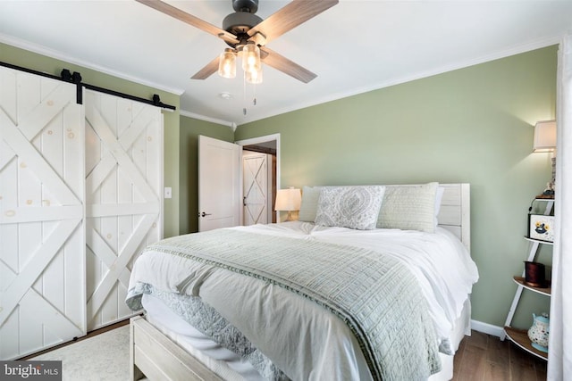 bedroom with a barn door, ornamental molding, a ceiling fan, wood finished floors, and baseboards