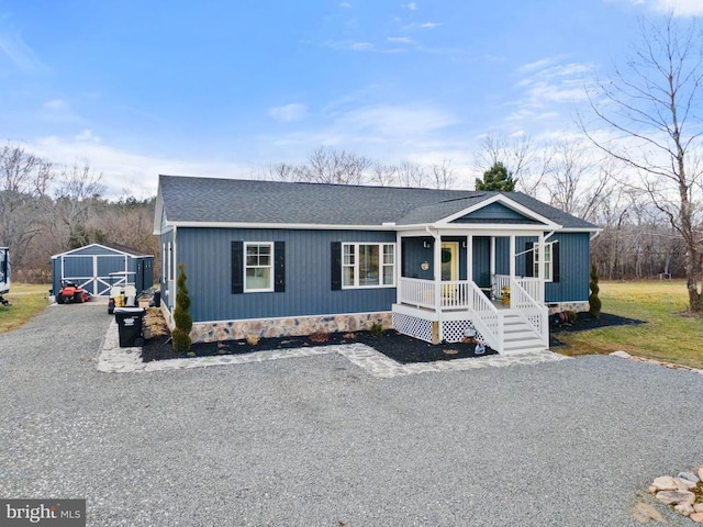 view of front of property with roof with shingles, gravel driveway, an outdoor structure, a porch, and a front yard