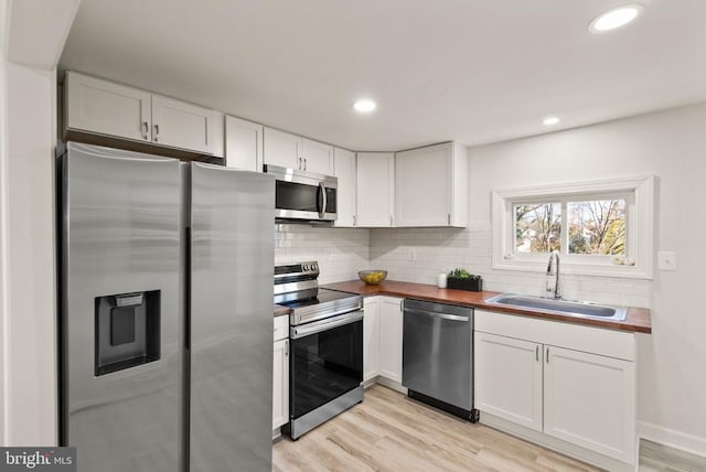 kitchen with tasteful backsplash, white cabinets, light wood-style flooring, appliances with stainless steel finishes, and a sink