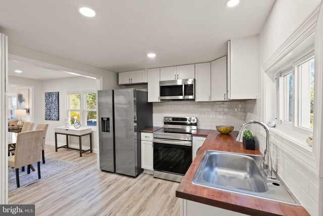 kitchen with light wood finished floors, tasteful backsplash, wood counters, stainless steel appliances, and a sink