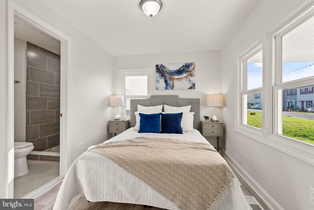 bedroom featuring ensuite bath, multiple windows, and baseboards